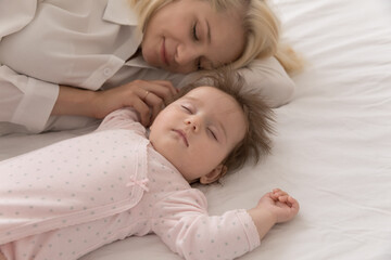 Close up above shot serene mother sleeping with infant daughter lying together on bed. Adorable babygirl looks carefree rest with loving mommy take healthy day nap at home. Maternity, babyhood concept
