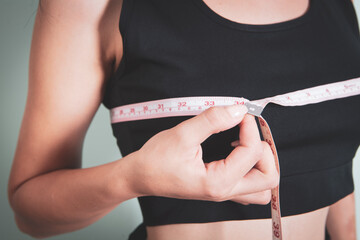 young girl measures breast girth on a gray background