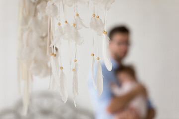 Close up white feather dreamcatcher amulet hanging in domestic room, on background silhouette of...
