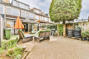 View of a two-story house and a courtyard with a lawn, chairs, tires, a trash can, a fence and a...