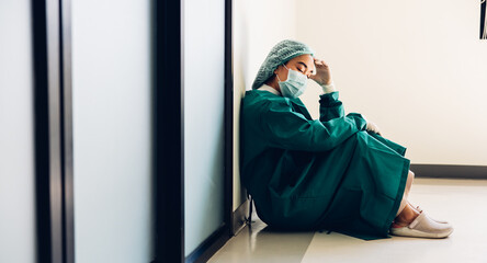 Tired depressed and sad feeling. Asian female surgeon doctor sitting on floor in font of operating room.