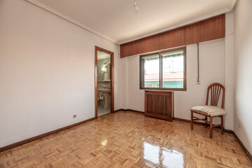 Room with a chair, wooden radiator cover, shiny oak parquet flooring and a brown aluminum window