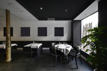Dining room of a restaurant with tableware set, window with plants and golden metal column