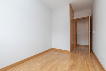 Empty bedroom with built-in wardrobe with oak doors matching the floor and plain white painted walls