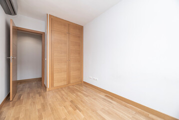 Empty bedroom with two door oak built in wardrobe, matching wooden flooring and white painted walls