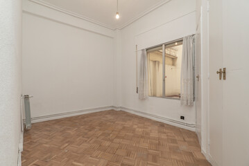 Empty living room with oak parquet and white carpentry, oak parquet floor, three-body built-in wardrobes with six doors and plain white painted walls with aluminum and glass window