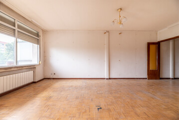Empty living room with oak flooring, woodwork and large window with white aluminum radiator below
