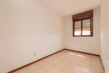 Empty room with stoneware floors with square tiles, reddish aluminum window and a lot of sun outside