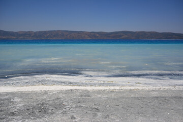 lake with blue light water and white sand and hills on horizon