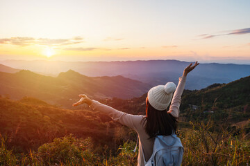 Happy young woman traveler relaxing and looking at the beautiful sunset on the top of mountain