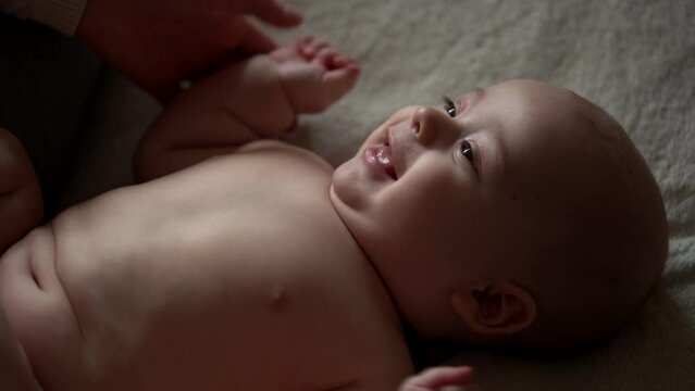 Newborn Baby And Young Mom Lie On Bed. Cute Smiling Teethless Kid Face Portrait. Woman Makes Massage Naked Child. Mother Care Of Babe. Infant, Mother Day, Childbirth, Beginning, Relationship Concept