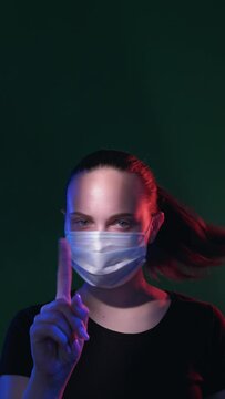 Warning gesture. Covid-19 risks. Worried woman in medicine mask blue red neon light glow waving finger looking at camera isolated on black vertical loop motion. Rejecting disagreement. New normal