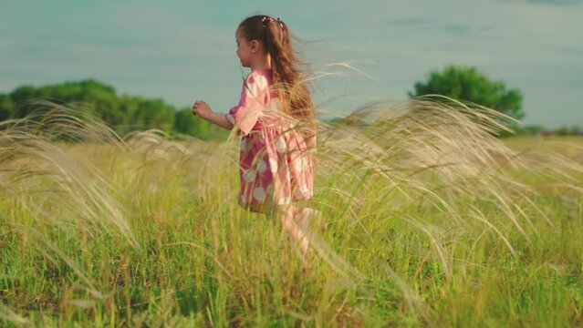 Kid runs across meadow, childhood dream. Happy family concept, child's dream. Little girl runs on grass, in sun, slow motion. Happy little girl playing at sunset. Happy child in field at sunset