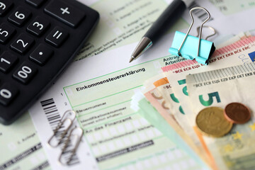 German income tax return form with pen and european euro money bills lies on accountant table close up. Taxpayers in Germany using euro currency to pay taxes