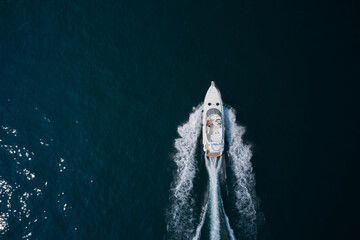 A large white boat at a speed of movement on the water leaves a white trail, top view. White yacht...