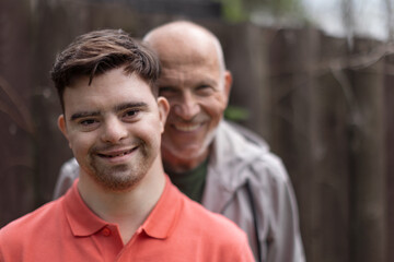 Portrait of happy senior father with his young son with Down syndrome outdoors. - obrazy, fototapety, plakaty