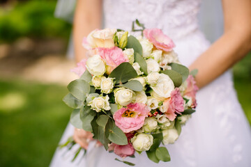 Obraz na płótnie Canvas Bride holds a wedding bouquet of white and pink roses on the green background outdoors in the open air, wedding dress, wedding details close-up view. High quality photo