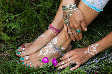 woman hands and bare feet with mandala drawing  on grass with lot jewrly rings bracelets summer day...