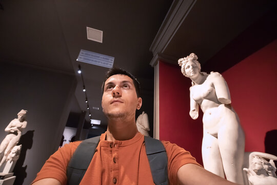 Man taking selfie photo in the hall with Greek antique statues of women and goddesses in the interiors of the Archaeological Museum in Antalya