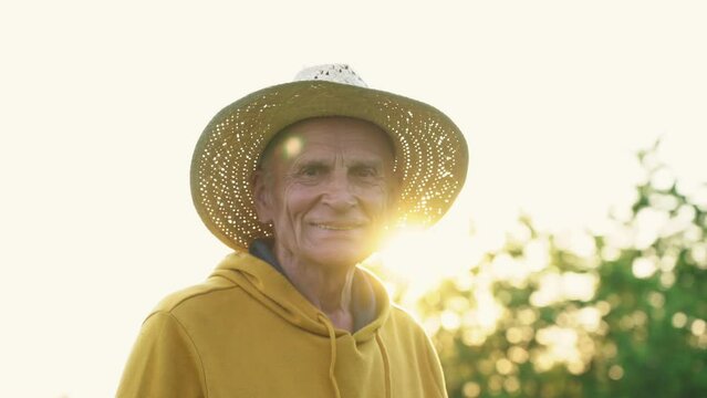 Older male person wearing big straw hat posing with smile on face standing outside at sunset
