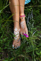 woman bare feet with mandala drawing  on grass with lot jewrly rings bracelets summer day close up