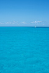 A sailboat on the horizon in the crystal clear tropical sea against the blue sky of a summer day. Travel vacations