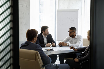 Team of serious multiracial businesspeople negotiating, solve business, search solution, seated at desk gathered in modern office boardroom. Teamwork, partnership, formal group meeting event concept