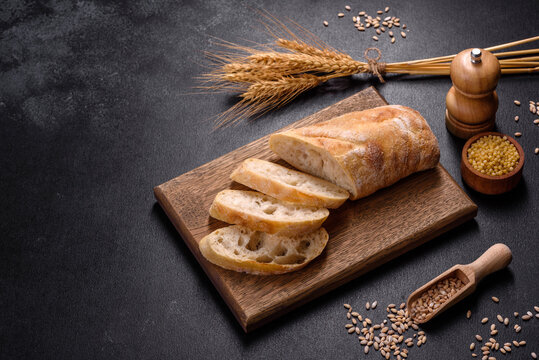 French baguette bread sliced on a wooden cutting board against a dark concrete background
