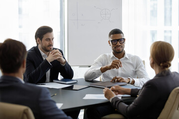 Millennial multinational businessmen take part in group formal meeting sit at desk in board room listen to female team leader looks interested. Negotiations, business, seminar event in office concept