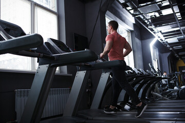 Rear view full length shot of a male bodybuilder doing cardio workout, running on treadmill - obrazy, fototapety, plakaty