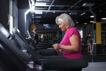 Fototapeta premium Happy healthy senior woman running on a treadmill at the gym