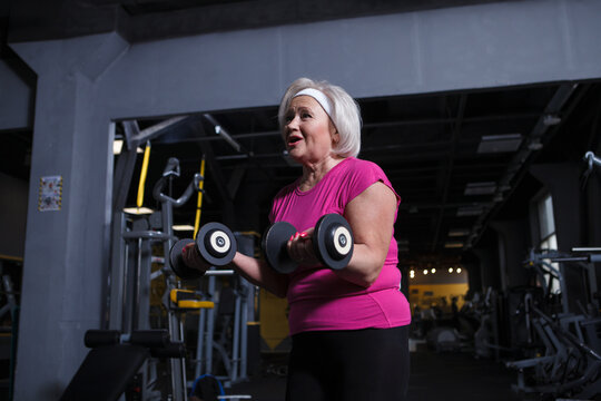 Cheerful Senior Woman Enjoying Working Out At The Gym, Doing Biceps Curls With Dumbbells