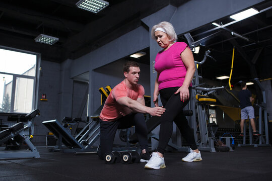 Senior woman doing lunges under personal trainer supervision at the gym