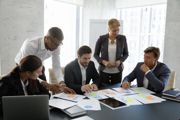 Group of diverse young and middle-aged teammate gather in office engaged in paperwork, making financial statistics review during briefing in modern boardroom. Negotiation, forecast, brainstorm concept