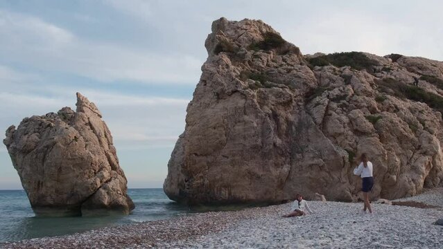 A woman takes a photo of another woman at the beach at the Petra tou Romiou rocks, in Paphos, Cyprus. The beach is considered to be Aphrodite's birthplace in Greek mythology.
