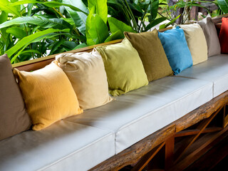 Row of many color of pillows decoration on the vintage wooden seat with white pads near the green...