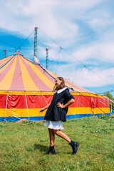 Beautiful woman in dress poses against backdrop of circus tent on sunny day