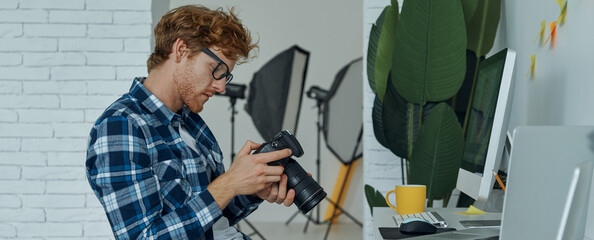 Handsome man examining camera while sitting at his working place in studio