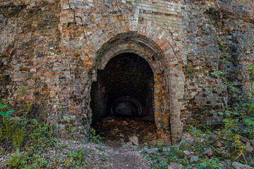 Obraz premium Military underground ruined brick tunnel entrance. Dark hole of subterranean grotto exit