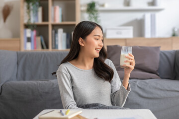 Healthy Young Asian woman Drinking milk with calcium for strong bone at home. Smiling indian woman...