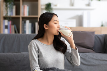 Healthy Young Asian woman Drinking milk with calcium for strong bone at home. Smiling indian woman...