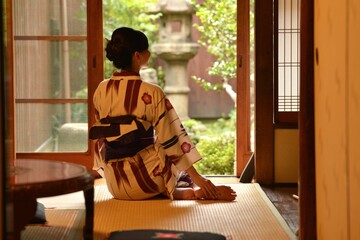 京都町屋の縁側に座りたたずむ浴衣を着た若く美しい女性の後ろ姿