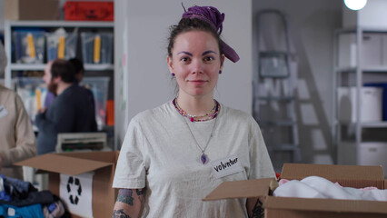 Young woman volunteer with purple hair and tattoos smiling at camera in military warehouse