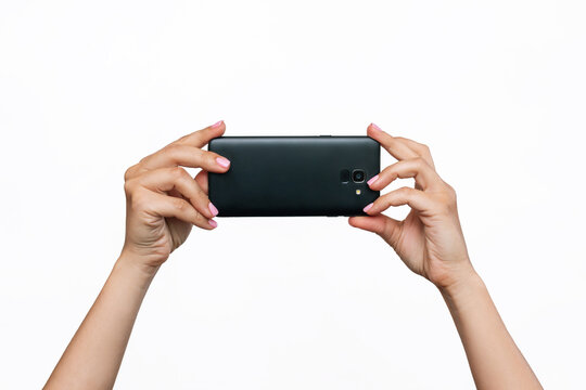 Mobile phone with photo camera in female hands isolated on a white background. Blank with an empty copy space for the design. Mockup of a smartphone. A young woman takes picture 