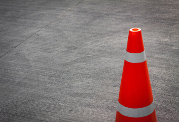 Striped orange cones on the asphalt road. Plastic orange cone on the road. Traffic cone on a parking lot in the park. traffic cone, with white and orange stripes on gray asphalt, copy space.