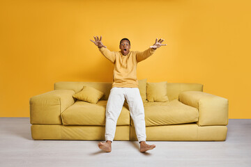 Excited mixed race man falling on the couch with yellow background