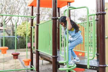 Horizontal image of a little African-American girl outdoors playing on a playground in a park.
