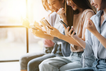 Groups of women sit in a row in the room, playing with cell phones. The concept of using a smartphone communication tool to play social media and send messages to talk to people through applications.