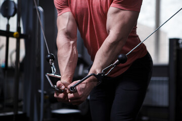 Cropped close up of muscular arms of bodybuilder exercising in cable crossover gym machine