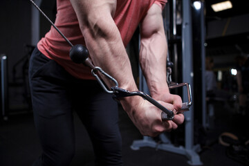 Muscular arms with veins close up, bodybuilder exercising in cable crossover gym machine